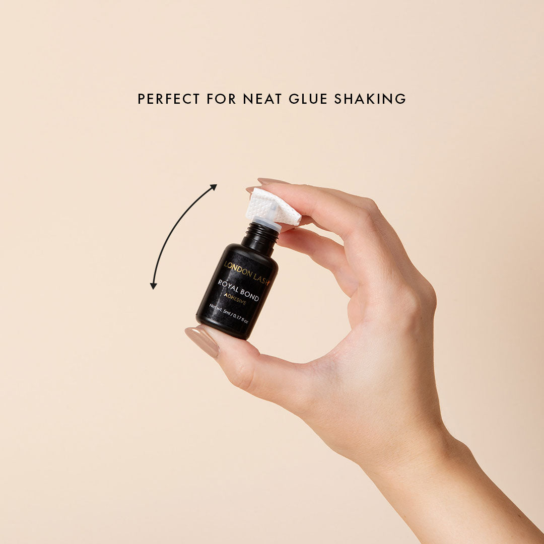 a bottle of lash extension glue held up with a glue nozzle wipe covering the open nozzle